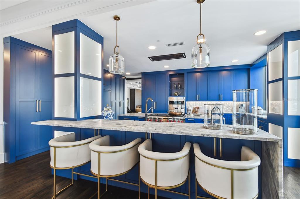 A kitchen features blue cabinetry, a marble-topped island, and four white bar stools — 450 KNIGHTS RUN AVENUE UNIT 2004, TAMPA, FL