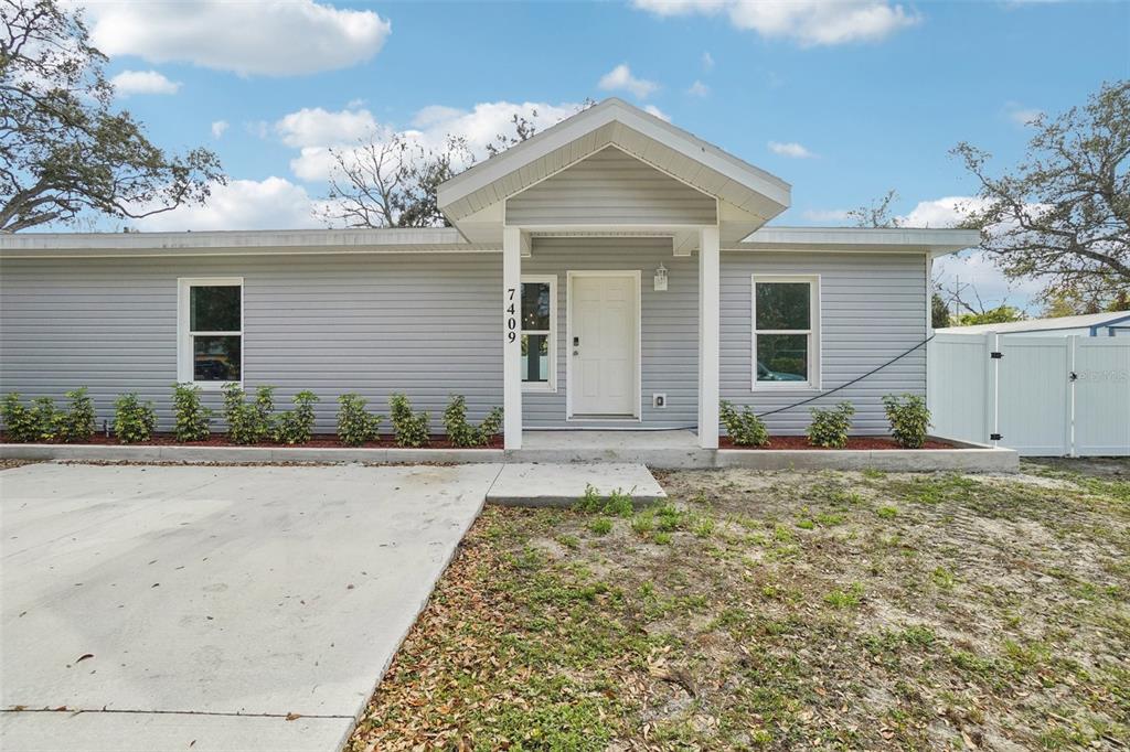 A single-story house with gray siding, a concrete driveway, and a covered front entryway — 7409 & 7411 E 23RD AVENUE, TAMPA, FL