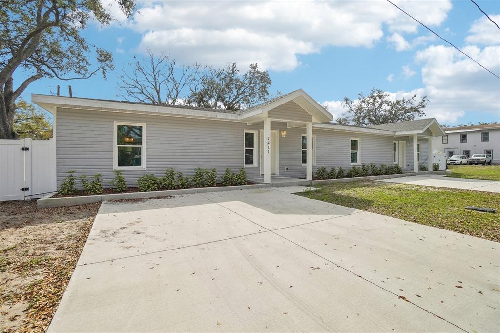 A single-story house with gray horizontal siding and a concrete driveway under a blue sky — 7409 & 7411 E 23RD AVENUE, TAMPA, FL