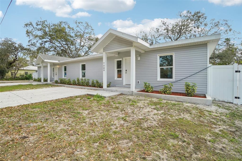 A single-story gray house with a concrete driveway and a white fence on the right — 7409 & 7411 E 23RD AVENUE, TAMPA, FL
