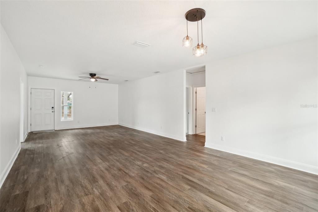 An empty living room features white walls, wood-look flooring, a ceiling fan, and pendant lighting — 7409 & 7411 E 23RD AVENUE, TAMPA, FL