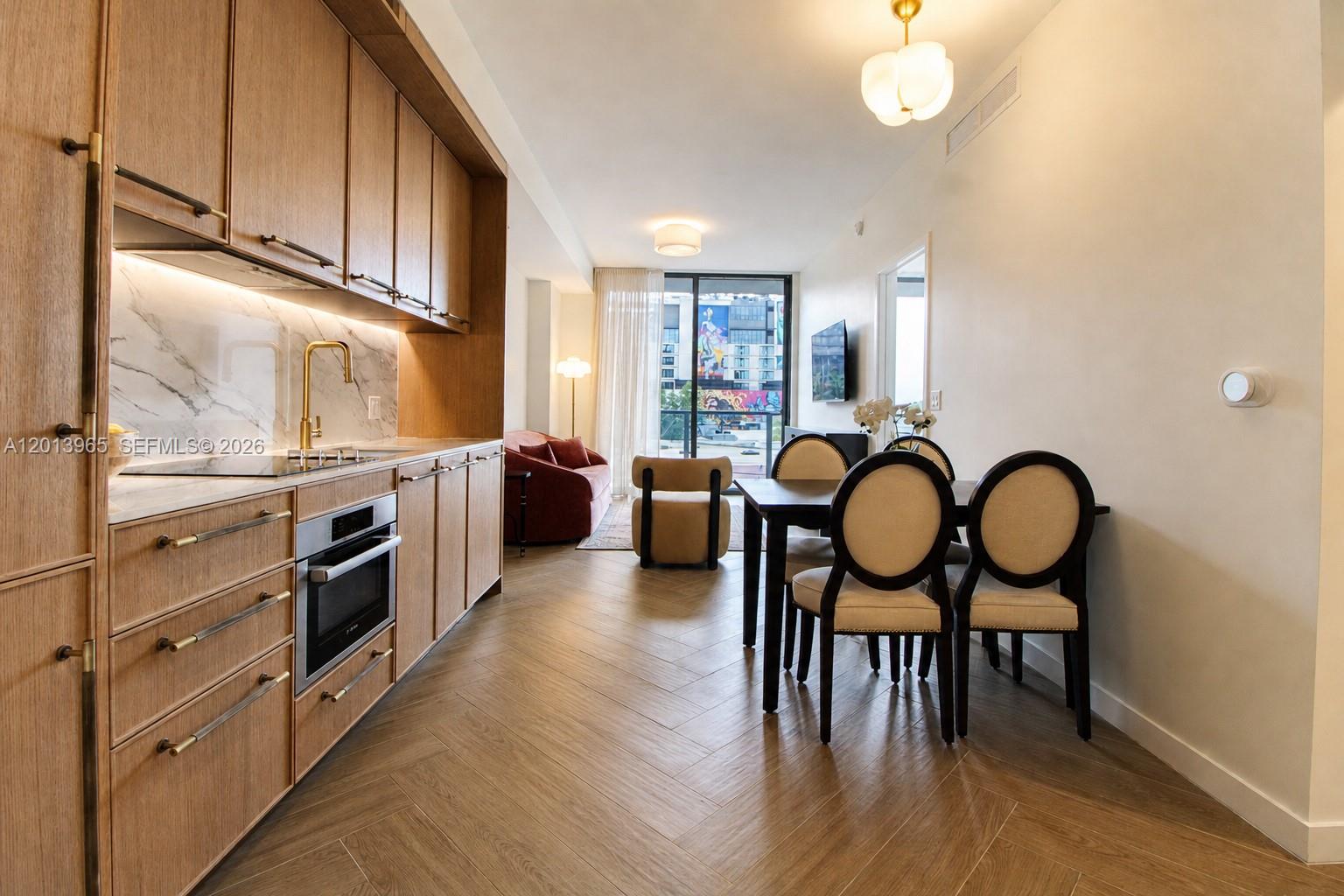 A modern kitchen and dining area feature wood cabinetry, herringbone flooring, and a balcony view — 2700 NW 2nd Ave # 202, Miami FL 33127, MIAMI, FL