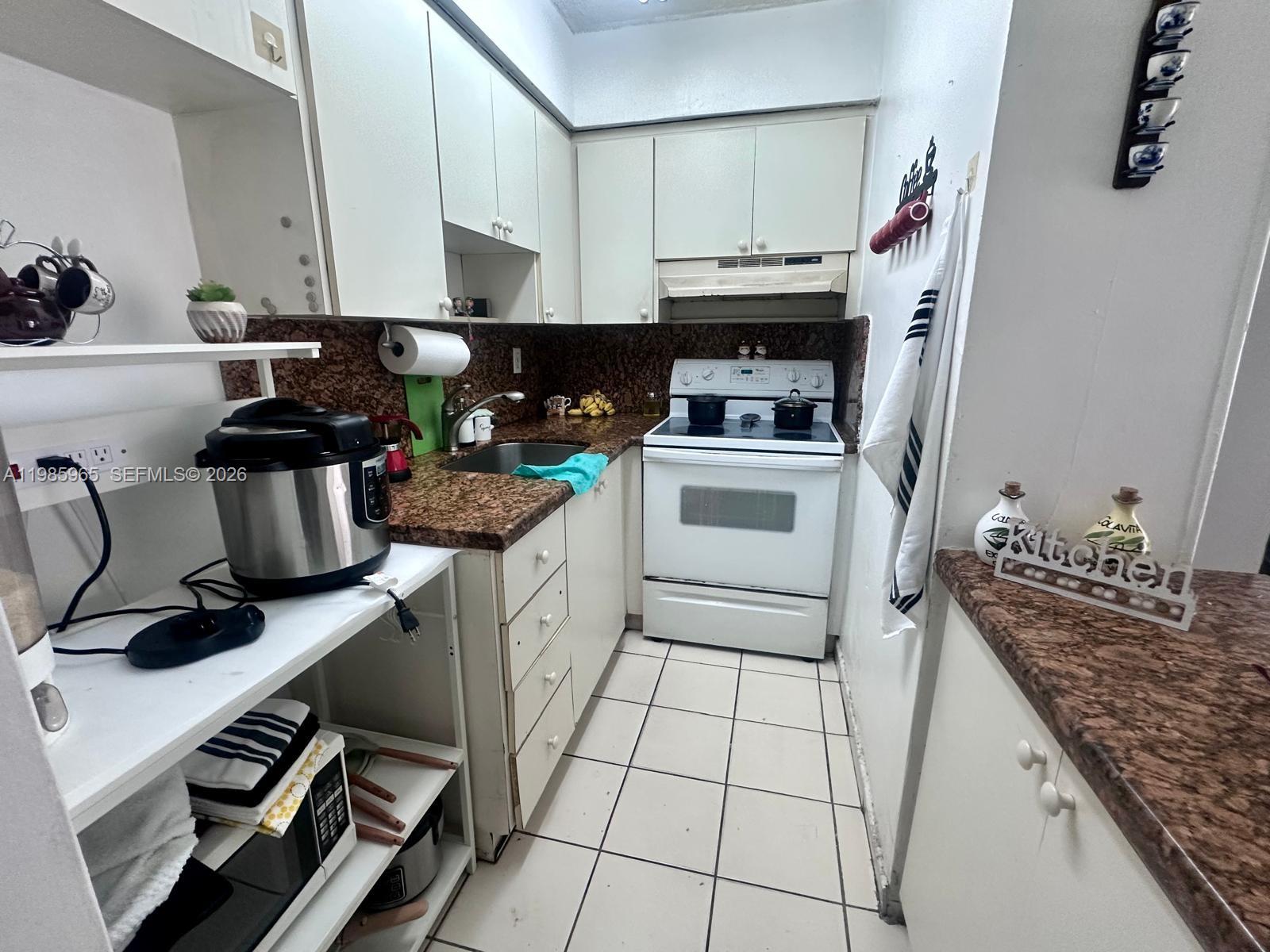 A galley kitchen features white cabinets, granite countertops, a white stove, and tiled flooring — 2385 NW 11th St # B16, Miami FL 33125, MIAMI, FL