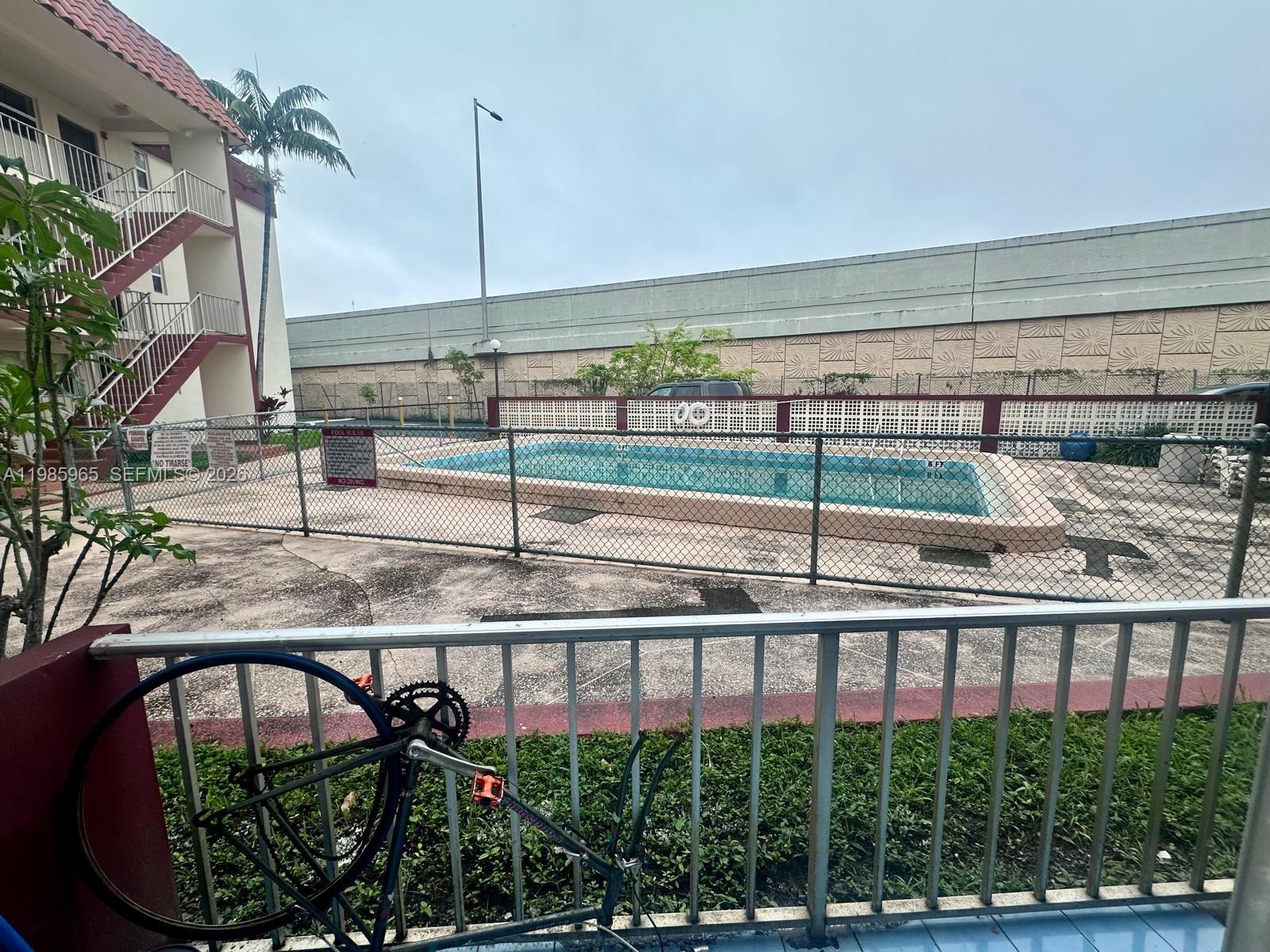 A view from a balcony overlooking a fenced-in swimming pool and a concrete wall — 2385 NW 11th St # B16, Miami FL 33125, MIAMI, FL