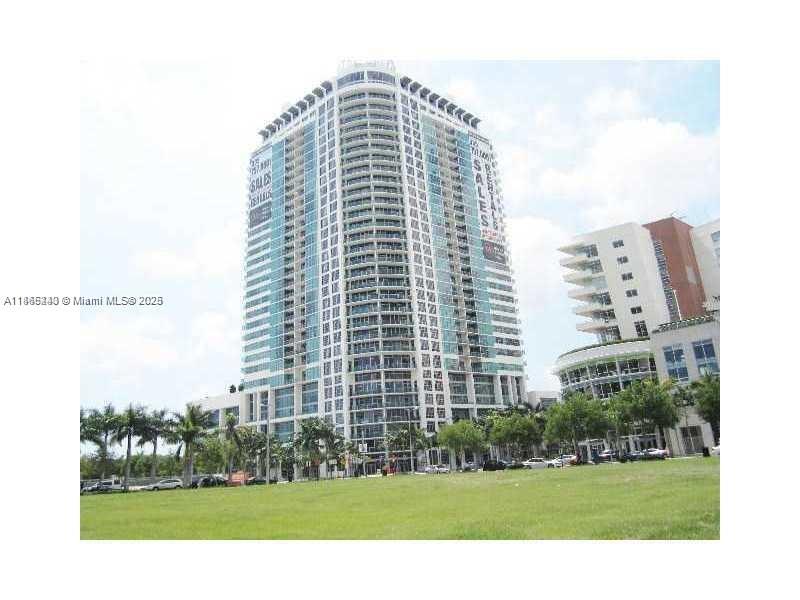 A tall, modern glass residential high-rise building stands next to a smaller building and lawn — 3301 NE 1st Ave # H2408, Miami FL 33137, MIAMI, FL