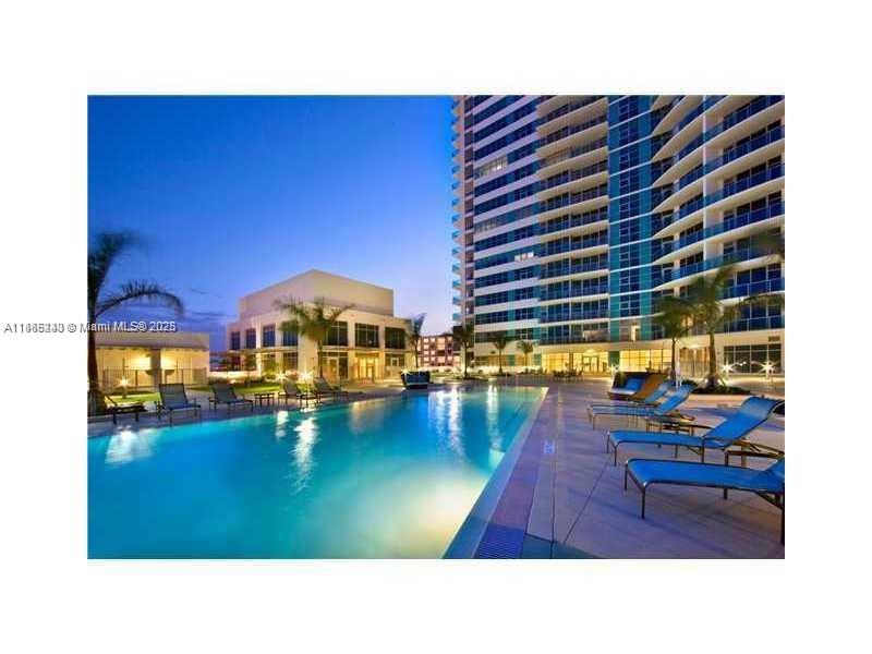 A swimming pool sits in front of a tall residential building at twilight — 3301 NE 1st Ave # H2408, Miami FL 33137, MIAMI, FL