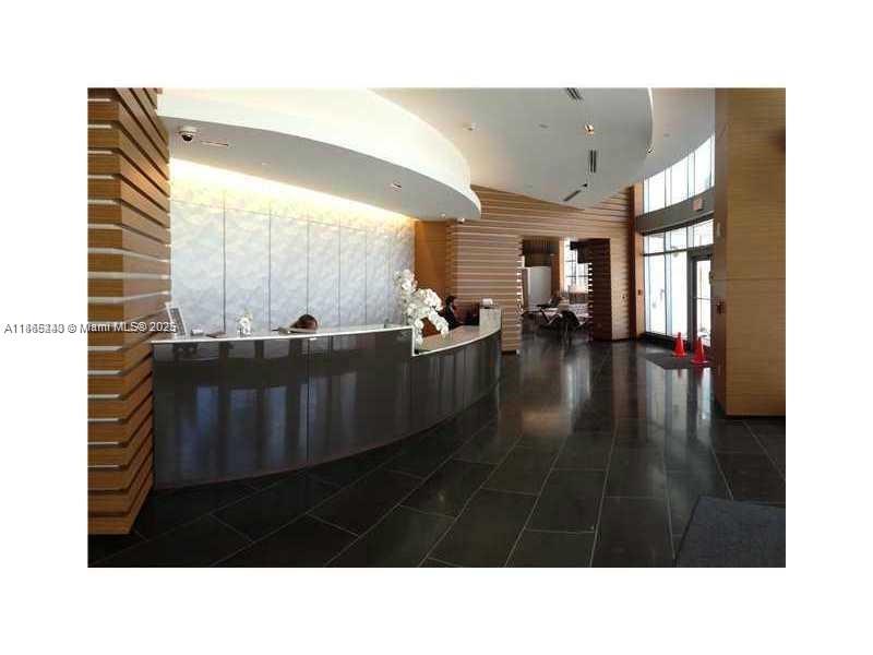 A modern lobby features a curved reception desk, wood-paneled walls, and dark tile flooring — 3301 NE 1st Ave # H2408, Miami FL 33137, MIAMI, FL