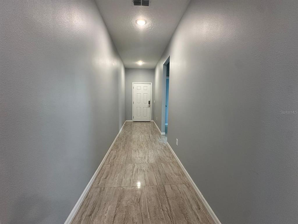 A hallway with gray walls, recessed lighting, and light-colored wood-look tile flooring leads to a door — 117 W MURPHY STREET, DAVENPORT, FL