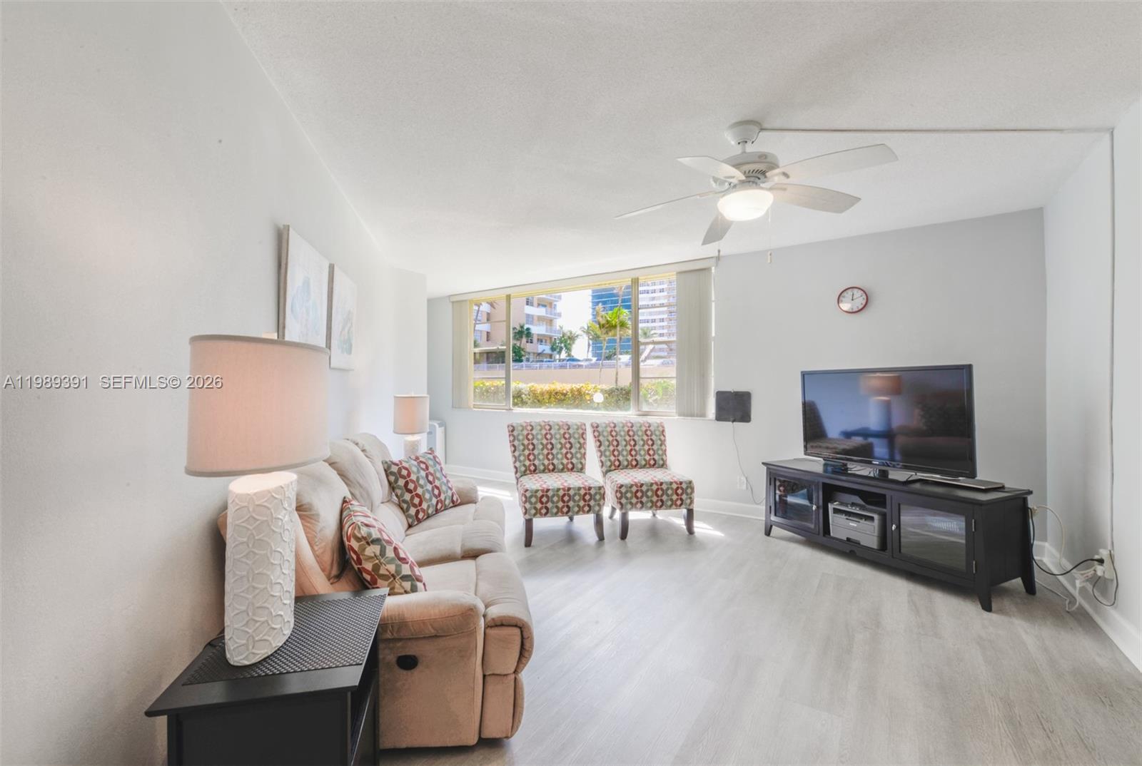 A living room features a beige sofa, two patterned chairs, a television, and light flooring — 1936 S Ocean Dr # 2D, Hallandale Beach FL 33009, HALLANDALE BEACH, FL