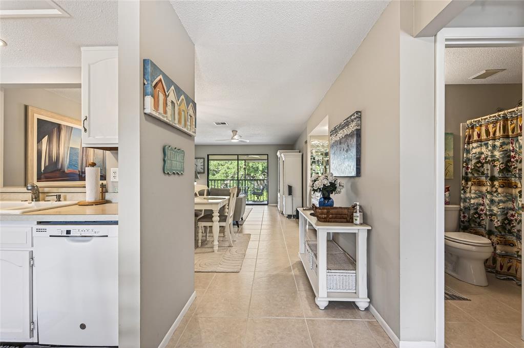 A hallway leads from a kitchen and bathroom toward a dining area and living room — 360 THREE LAKES LANE UNIT J, VENICE, FL