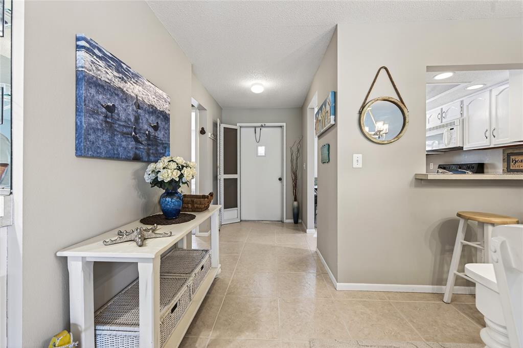 A tiled entryway features a white console table, wall art, and a view of the kitchen — 360 THREE LAKES LANE UNIT J, VENICE, FL