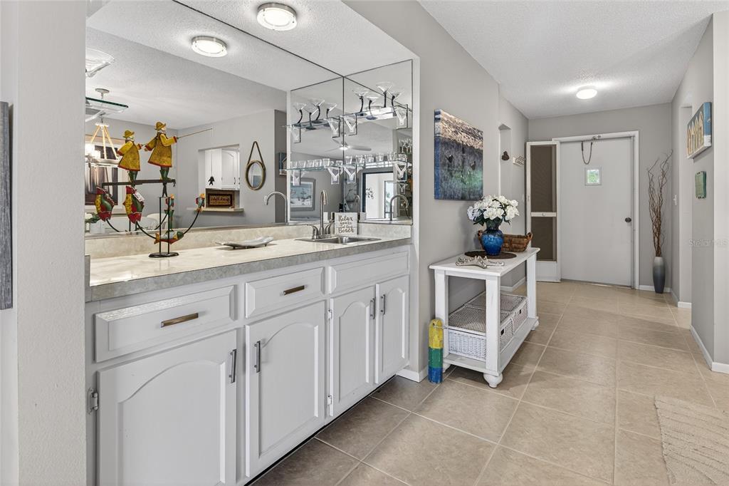 A wet bar with white cabinets and a mirror sits in a hallway near an entryway — 360 THREE LAKES LANE UNIT J, VENICE, FL