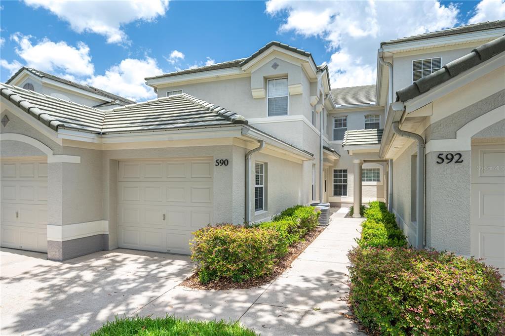 The exterior view shows two adjacent townhome units with beige stucco walls and tiled roofs — 590 GRASSLANDS VILLAGE CIRCLE UNIT 590, LAKELAND, FL