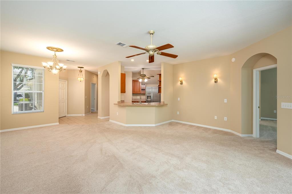 A carpeted living room opens to a kitchen with a breakfast bar and ceiling fans — 590 GRASSLANDS VILLAGE CIRCLE UNIT 590, LAKELAND, FL