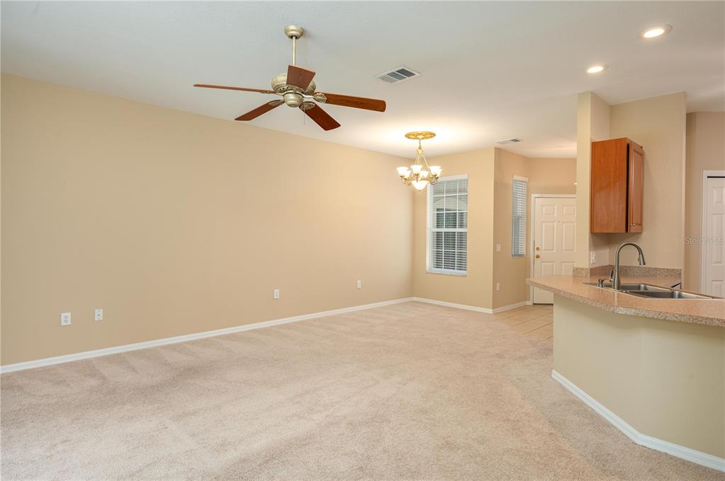 A carpeted living room with a ceiling fan flows into a kitchen with a breakfast bar — 590 GRASSLANDS VILLAGE CIRCLE UNIT 590, LAKELAND, FL