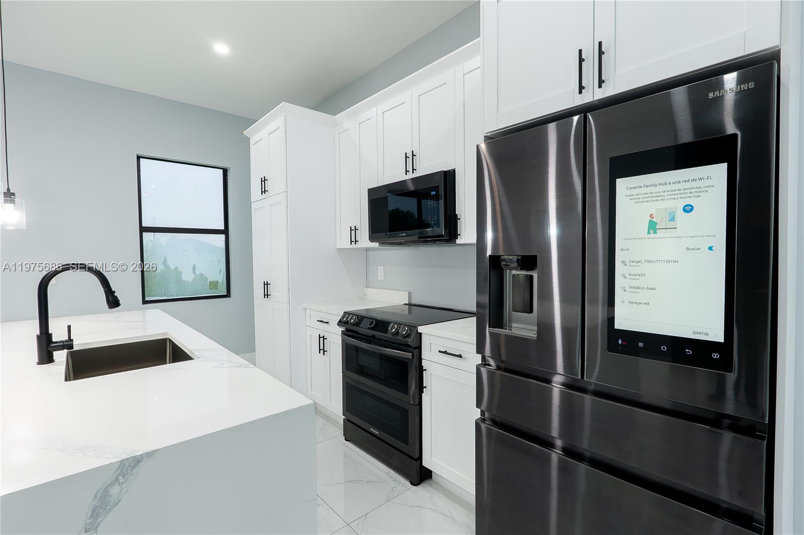 A modern kitchen features white cabinetry, a marble-topped island, and stainless steel appliances — 4703 elva ave s, Lehigh Acres FL 33976, LEHIGH ACRES, FL