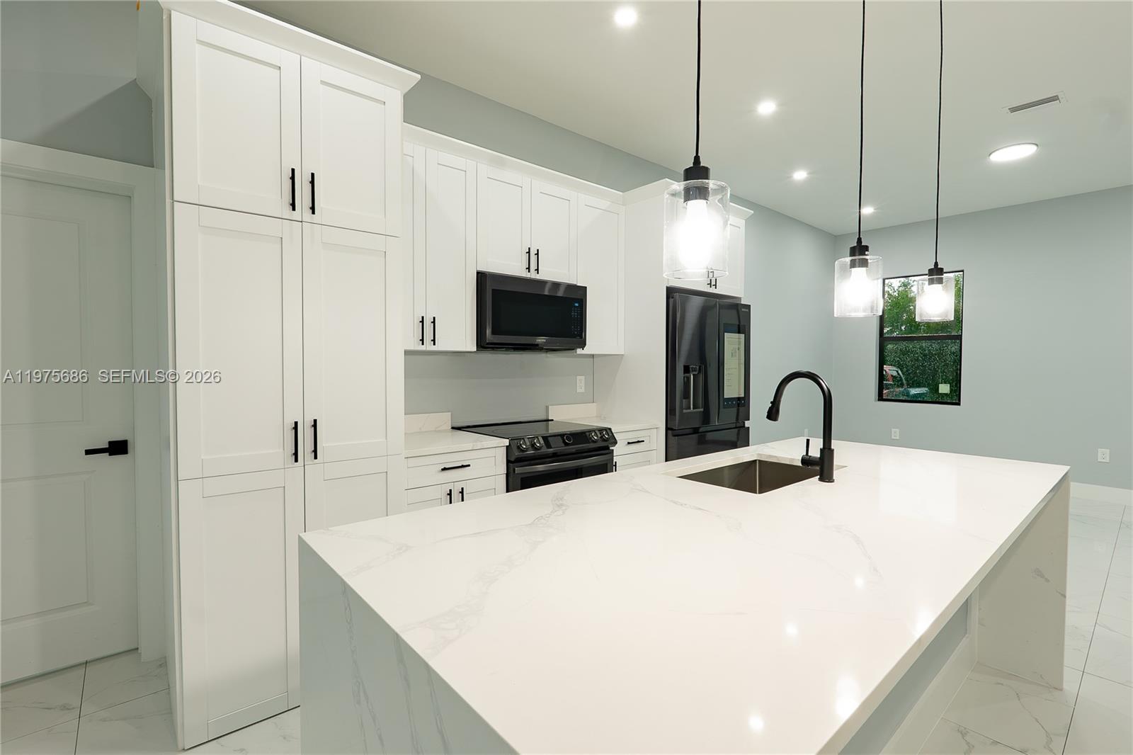 A modern kitchen features white cabinetry, a marble-topped island, and black fixtures — 4703 elva ave s, Lehigh Acres FL 33976, LEHIGH ACRES, FL