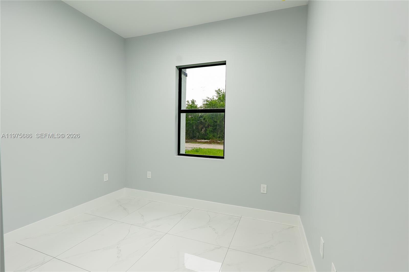 An empty room features light gray walls, white marble-look tile flooring, and a single window — 4703 elva ave s, Lehigh Acres FL 33976, LEHIGH ACRES, FL