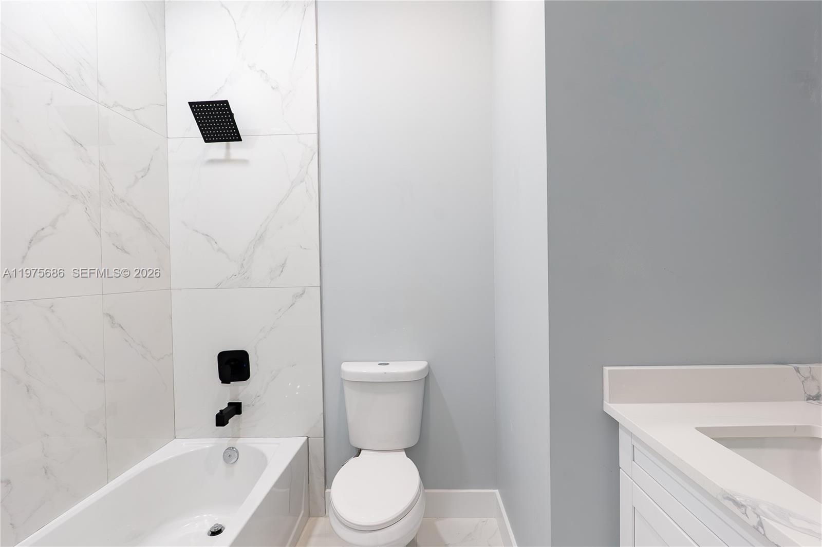 A bathroom features a white marble-tiled shower, a toilet, and a white vanity — 4703 elva ave s, Lehigh Acres FL 33976, LEHIGH ACRES, FL