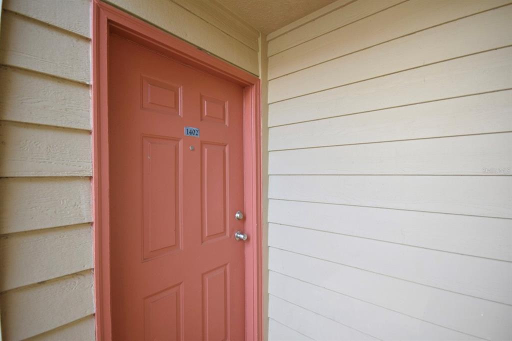 A salmon-colored front door with the number 1402 is set against light-colored horizontal siding — 9481 HIGHLAND OAK DRIVE UNIT 1402, TAMPA, FL