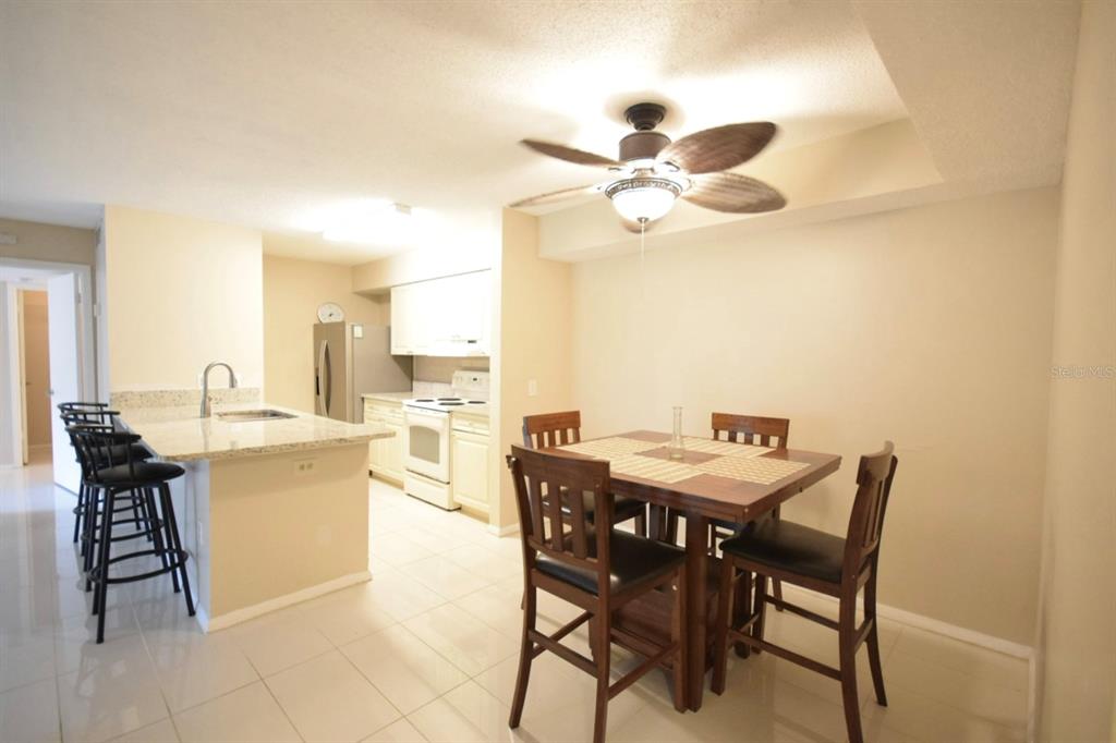 A kitchen with light cabinets and granite countertops opens to a dining area with seating — 9481 HIGHLAND OAK DRIVE UNIT 1402, TAMPA, FL