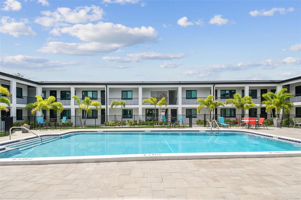 A rectangular swimming pool sits in front of a two-story apartment building with palm trees — 2942 W BAY DRIVE UNIT 2, BELLEAIR BLUFFS, FL