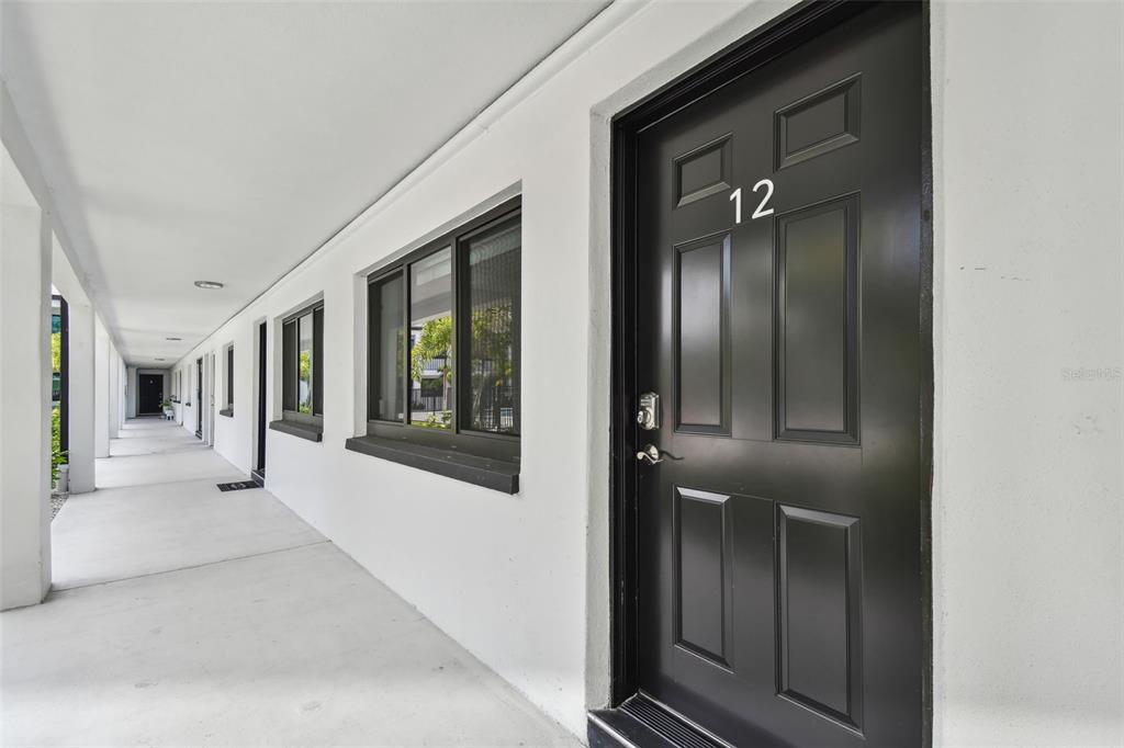 A black front door labeled 12 opens onto a covered outdoor walkway with white walls — 2942 W BAY DRIVE UNIT 2, BELLEAIR BLUFFS, FL