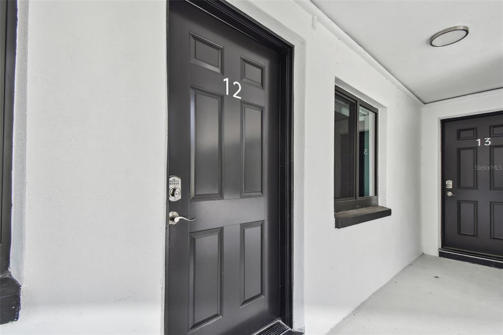 This exterior view shows two black apartment doors labeled 12 and 13 on a walkway — 2942 W BAY DRIVE UNIT 2, BELLEAIR BLUFFS, FL