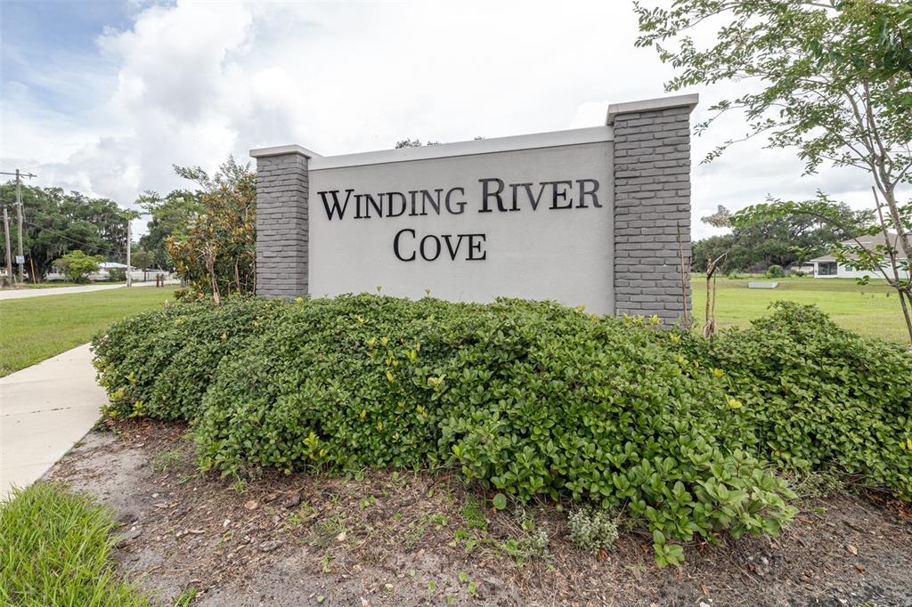 A gray monument sign for Winding River Cove stands behind a large green shrub — 2118 HADLEY RD, BARTOW, FL