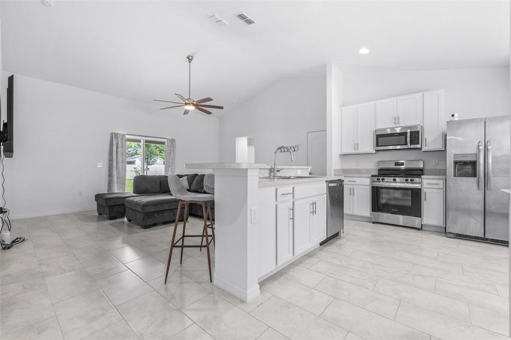 An open-concept kitchen and living area featuring white cabinets, stainless steel appliances, and tile flooring — 2118 HADLEY RD, BARTOW, FL