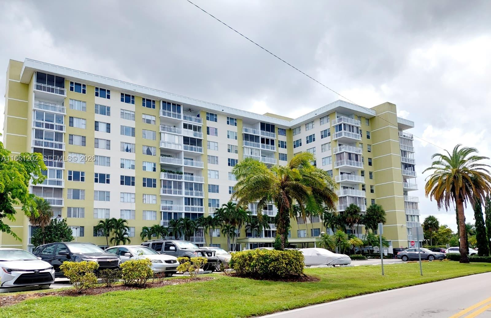 A multi-story apartment building with balconies and a parking lot sits behind a grassy lawn — 4400 Hillcrest Dr # 1005A, Hollywood FL 33021, HOLLYWOOD, FL