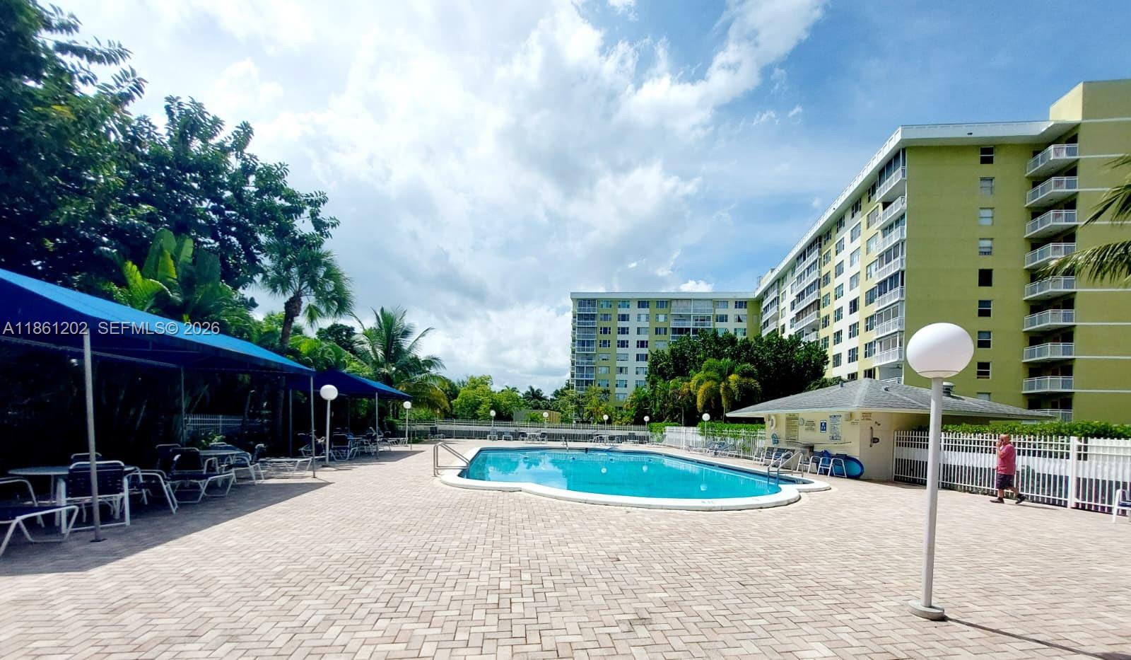 A swimming pool is surrounded by a paved patio, lounge chairs, and large apartment buildings — 4400 Hillcrest Dr # 1005A, Hollywood FL 33021, HOLLYWOOD, FL