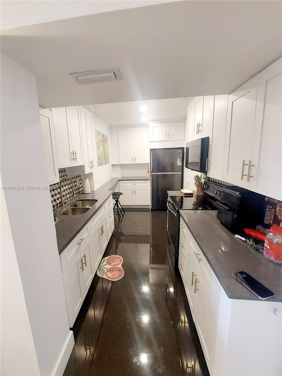 A galley kitchen features white cabinets, dark countertops, and a glossy dark floor — 4400 Hillcrest Dr # 1005A, Hollywood FL 33021, HOLLYWOOD, FL