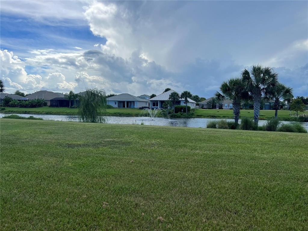A grassy lawn overlooks a pond with a fountain and houses in the background — 108 LONGVIEW WAY N, PALM COAST, FL