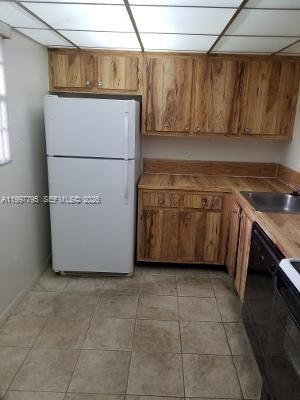 A kitchen features wood cabinets, a white refrigerator, and tiled flooring under a drop ceiling — 10425 SW 112th Ave # 211, Miami FL 33176, MIAMI, FL