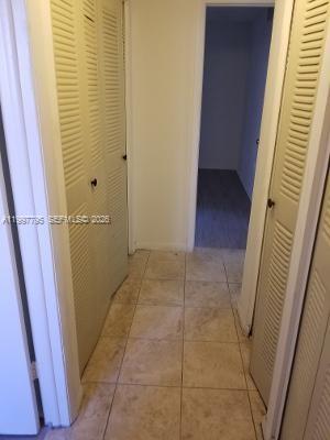 A hallway with beige tile flooring features louvered closet doors on both sides — 10425 SW 112th Ave # 211, Miami FL 33176, MIAMI, FL