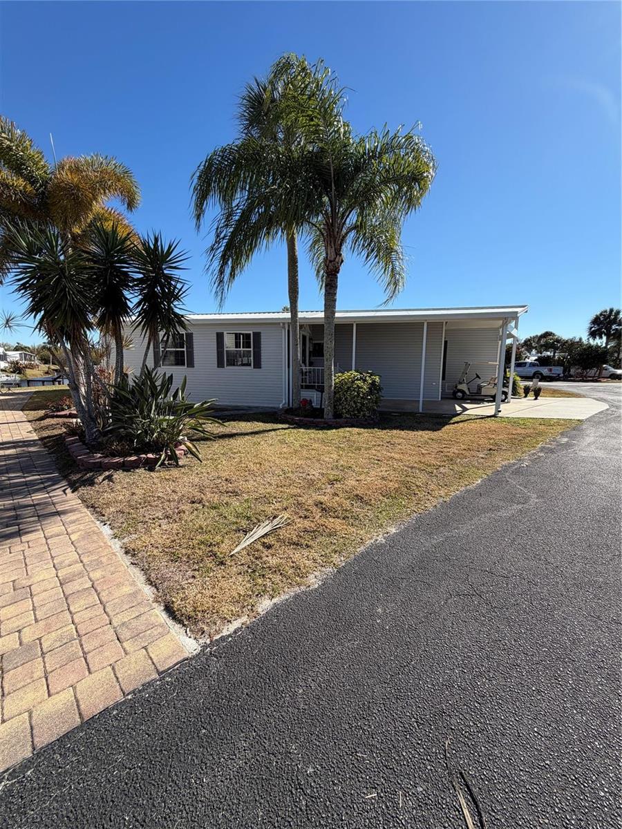 A single-story manufactured home features light siding, a covered carport, and palm trees — 12470 SE 140th Road, Okeechobee FL 34974, OKEECHOBEE, FL