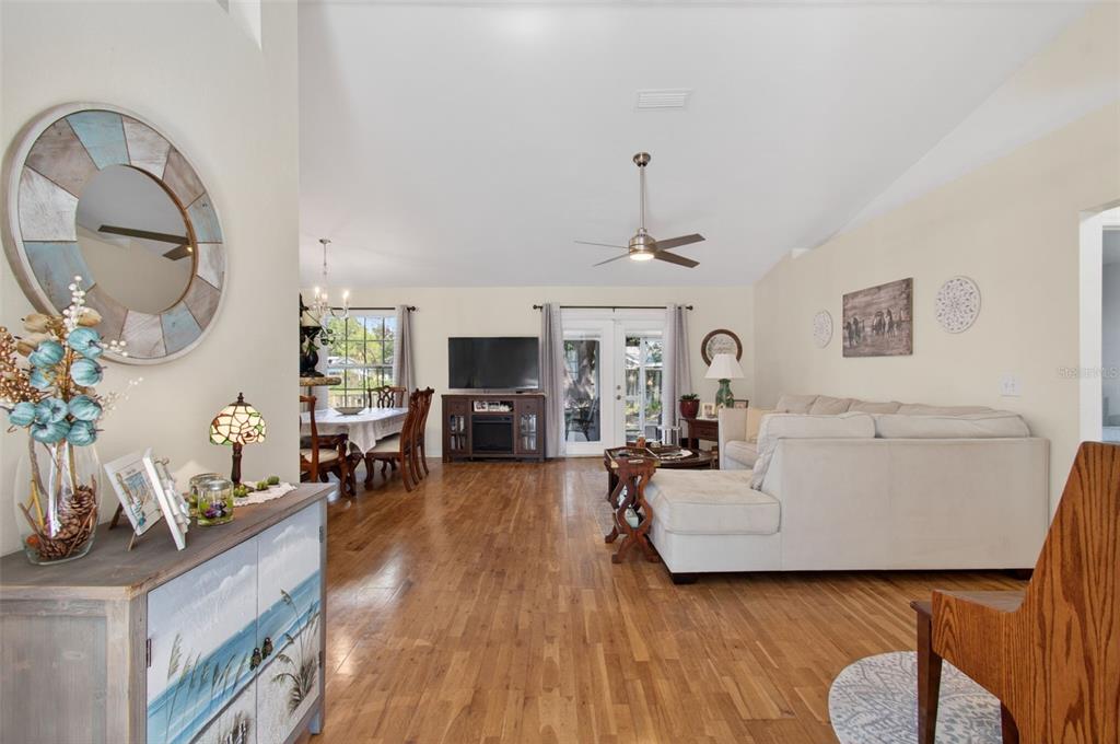 A living room with hardwood floors, a vaulted ceiling, and a dining area in the background — 6146 NW 38TH TERRACE, GAINESVILLE, FL