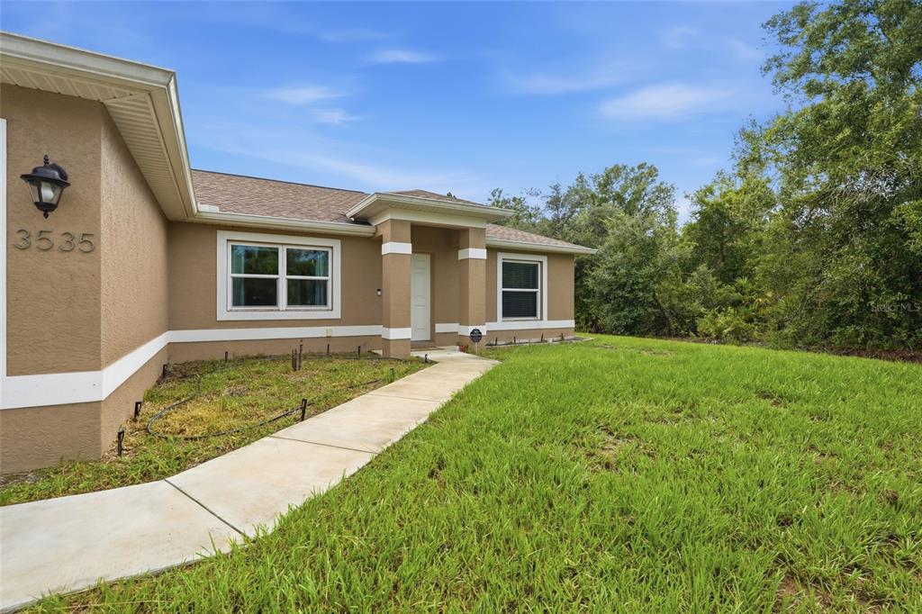A tan single-story house exterior features a concrete walkway leading to a recessed front entrance — 3535 SHAWNEE TERRACE, NORTH PORT, FL
