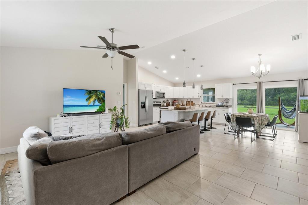 A spacious open-concept living room and kitchen featuring tile floors, vaulted ceilings, and sliding doors — 3535 SHAWNEE TERRACE, NORTH PORT, FL