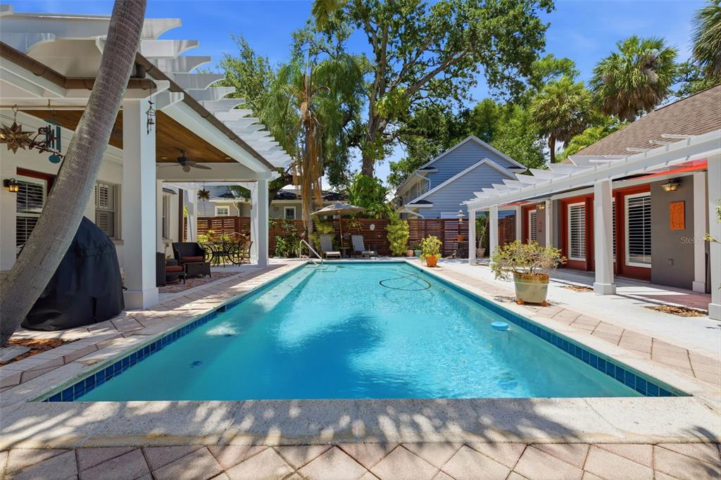A rectangular swimming pool sits between two covered patios with white pergolas in a backyard — 912 S FREMONT AVENUE, TAMPA, FL