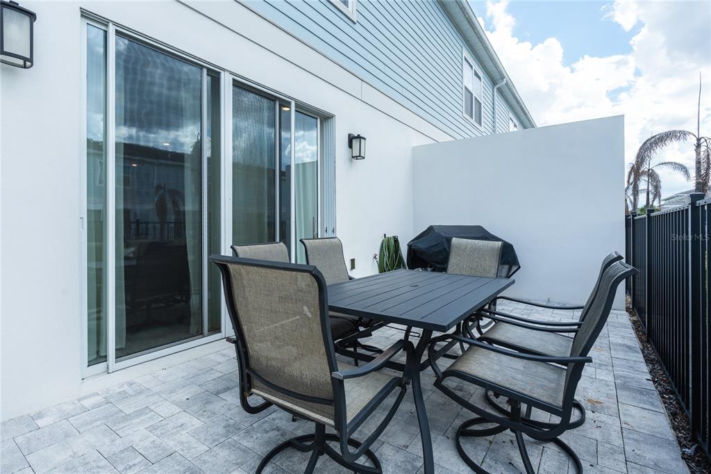 A patio with a dining set and grill sits outside a house with sliding doors — 7901 PUTTING WAY, KISSIMMEE, FL