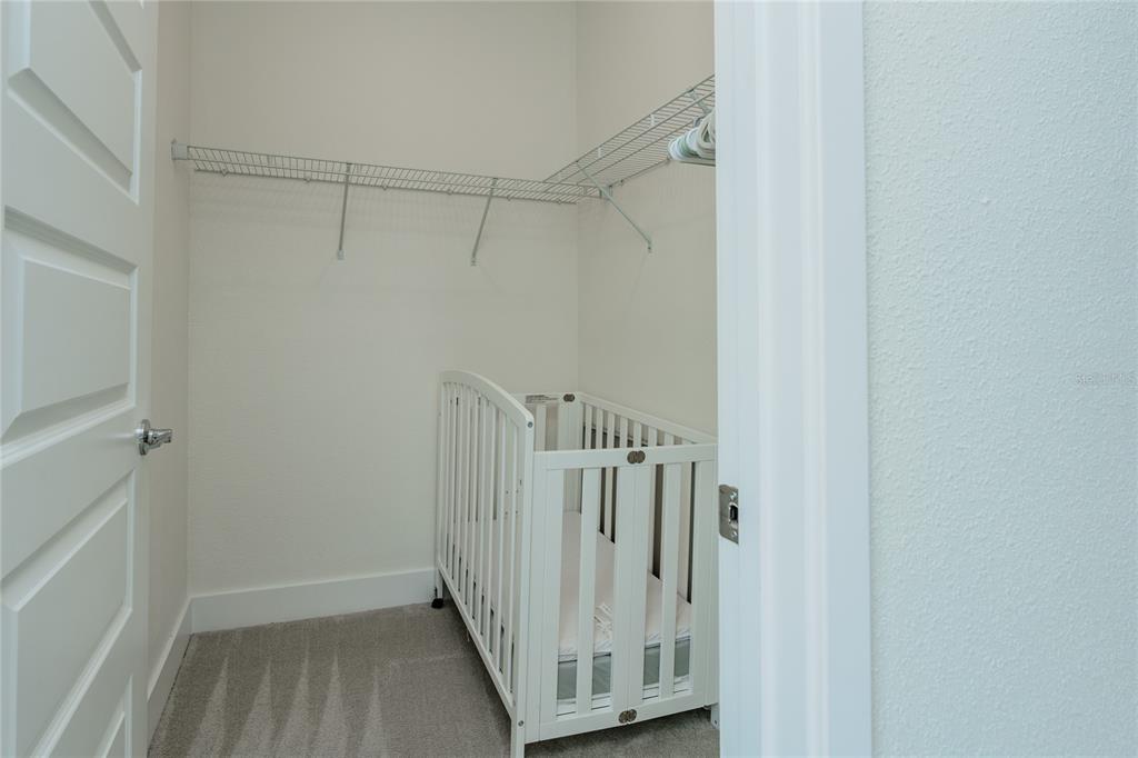 A white crib sits inside a small walk-in closet with wire shelving and carpeted flooring — 7901 PUTTING WAY, KISSIMMEE, FL