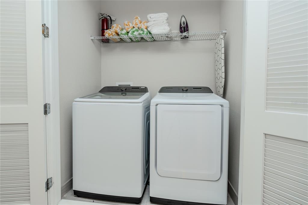 A laundry closet contains a white washer and dryer with a wire shelf above — 7901 PUTTING WAY, KISSIMMEE, FL