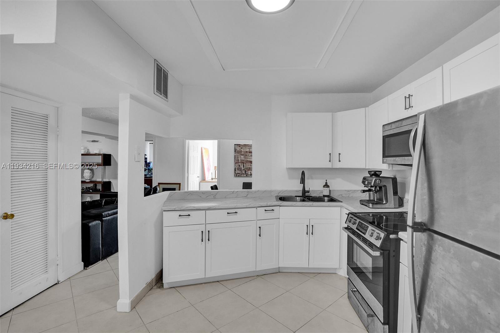 A kitchen features white cabinets, marble-look countertops, stainless steel appliances, and tile flooring — 1780 NE 191st St # 2, Miami FL 33179, MIAMI, FL
