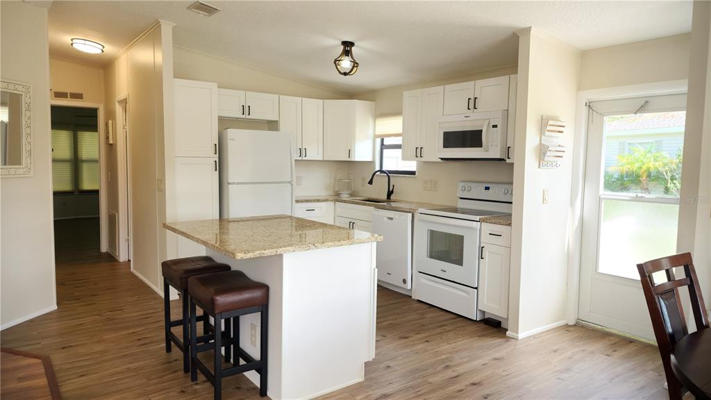 A kitchen with white cabinets, granite countertops, a center island, and wood-look flooring — 2100 KINGS HIGHWAY UNIT 956A, PORT CHARLOTTE, FL