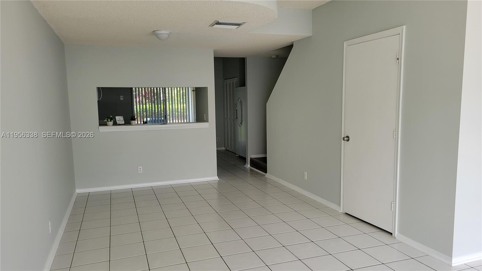 A room with light gray walls, white tile flooring, and a pass-through window to the kitchen — 16679 Hemingway Dr, Weston FL 33326, WESTON, FL