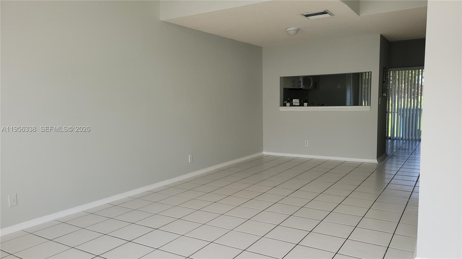 An empty room features light gray walls, white tile flooring, and a kitchen pass-through window — 16679 Hemingway Dr, Weston FL 33326, WESTON, FL