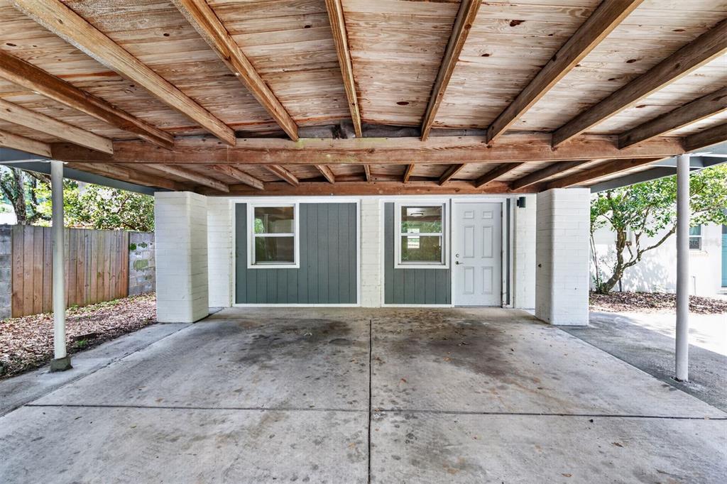 A covered carport with a concrete floor, wooden ceiling beams, and a white exterior wall — 2707 NW 4TH AVENUE, GAINESVILLE, FL