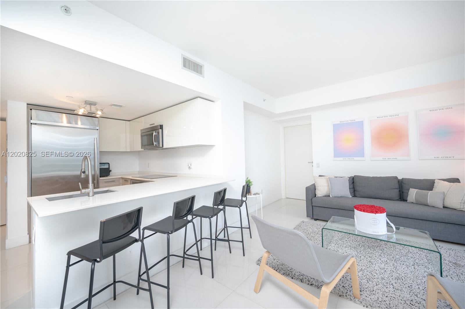 A modern kitchen with white cabinets and a breakfast bar opens into a living area — 1300 Brickell Bay Dr # 1601, Miami FL 33131, MIAMI, FL